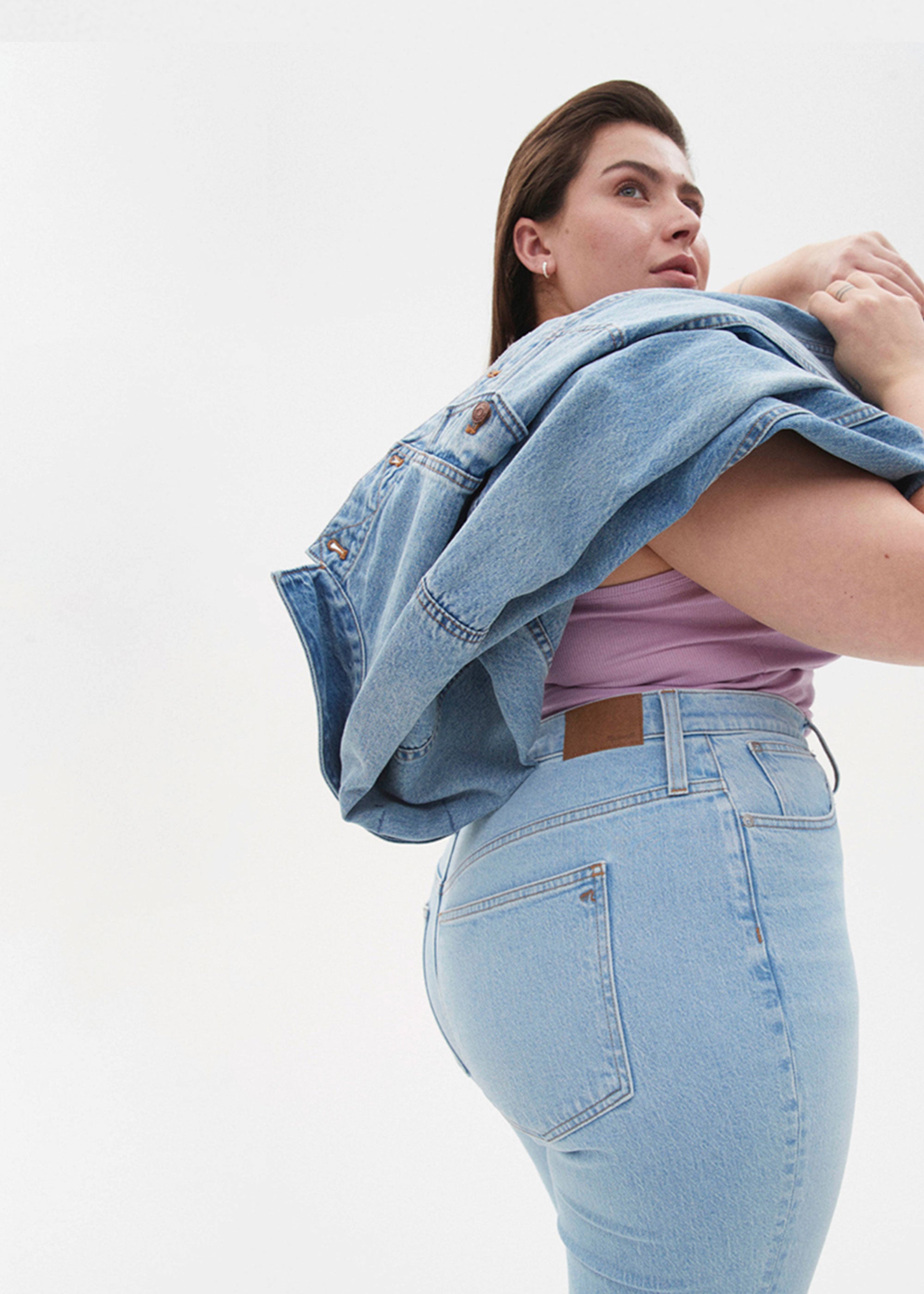 Individual wearing Madewell jeans and a lavender tank top, slinging a Madewell denim jacket over their shoulder